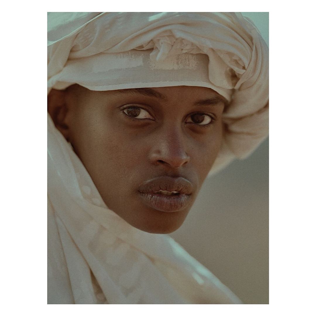 Close-up portrait of a dark-skinned adult woman with a white headscarf looking directly at the camera with a neutral expression.
