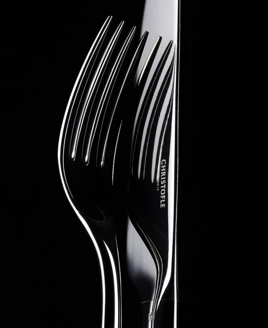 Close-up studio shot of a silver Christofle knife and fork. The lighting is high contrast and emphasizes the shiny metal of the utensils.