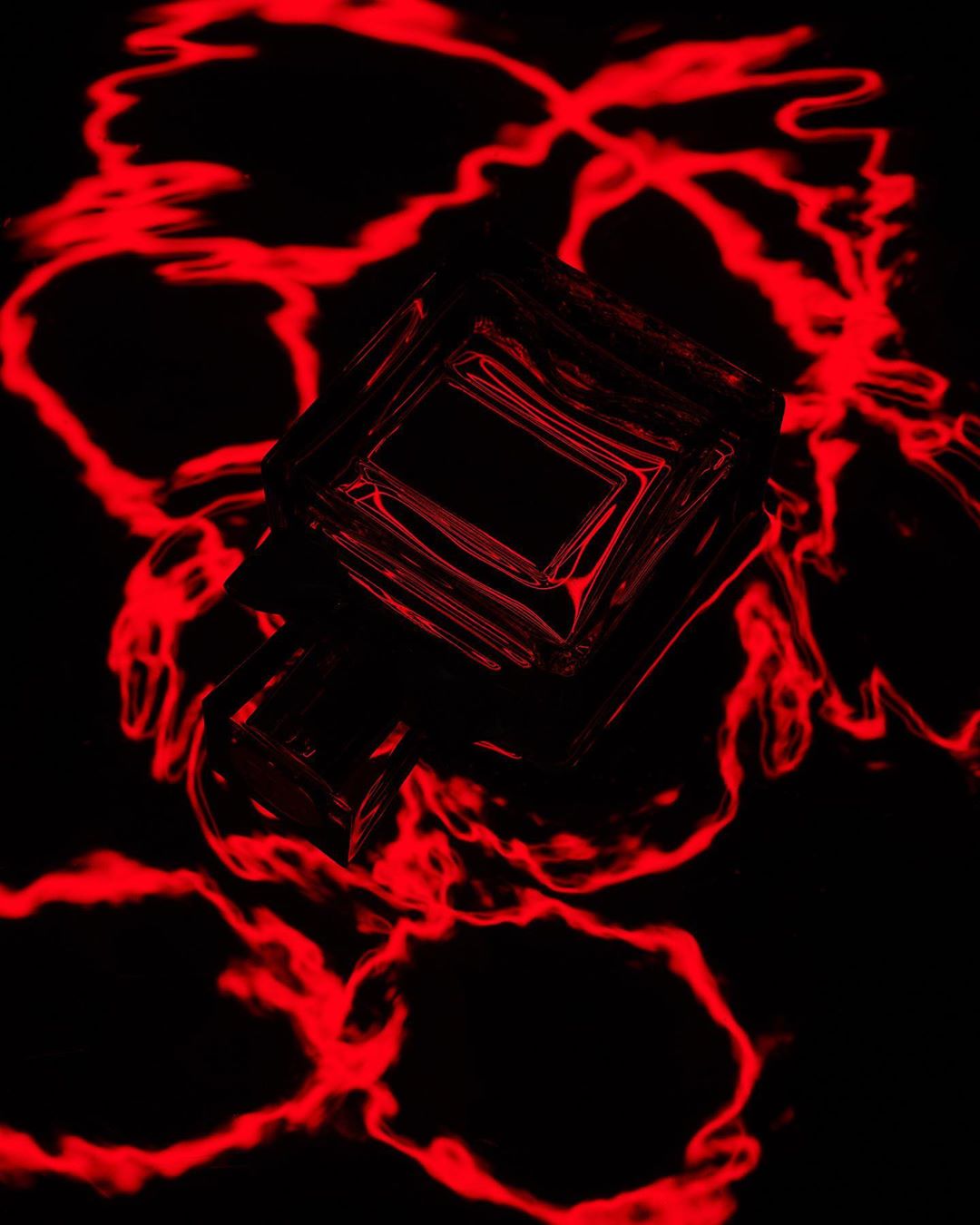Abstract shot of a clear cube with red light reflecting around it on a dark surface, creating a modern and artistic visual.