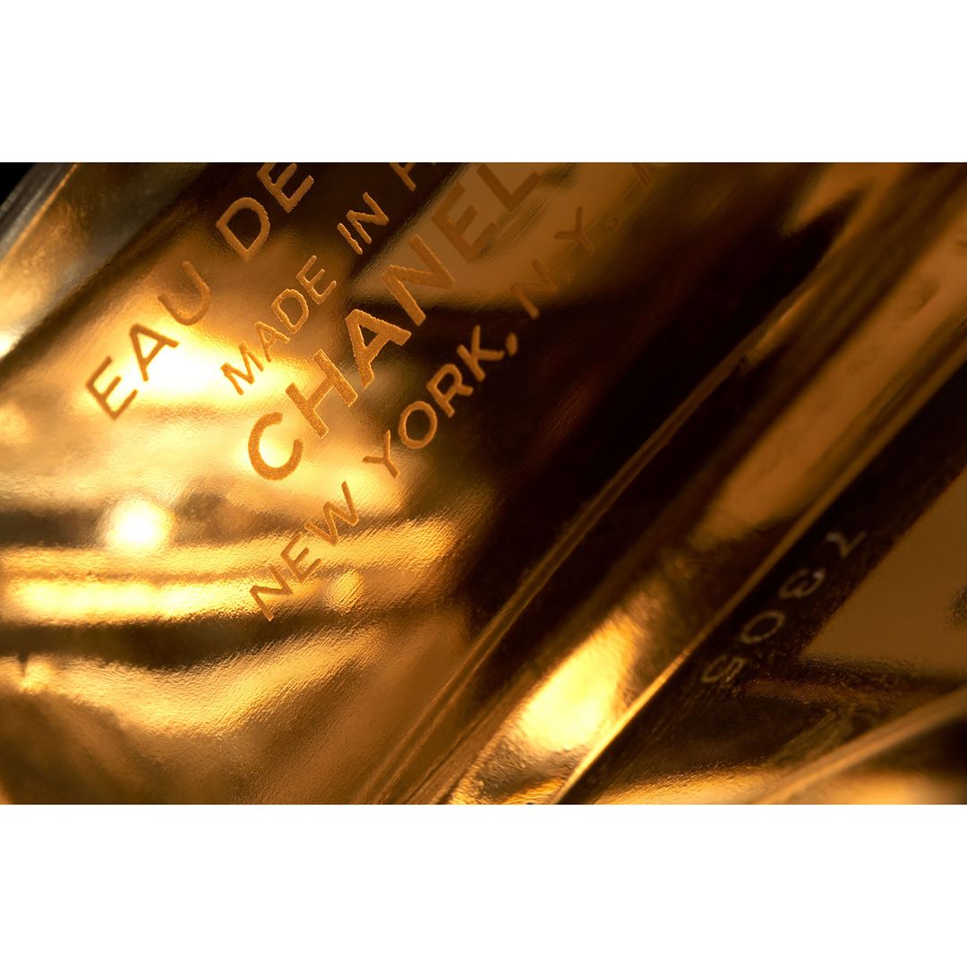 Close-up studio shot of amber-colored Chanel perfume bottle with embossed logo and text, reflecting studio lighting.
