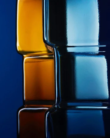 Stack of square-shaped glass bottles with amber and blue hues, shot against a dark blue background, creating sleek reflections.