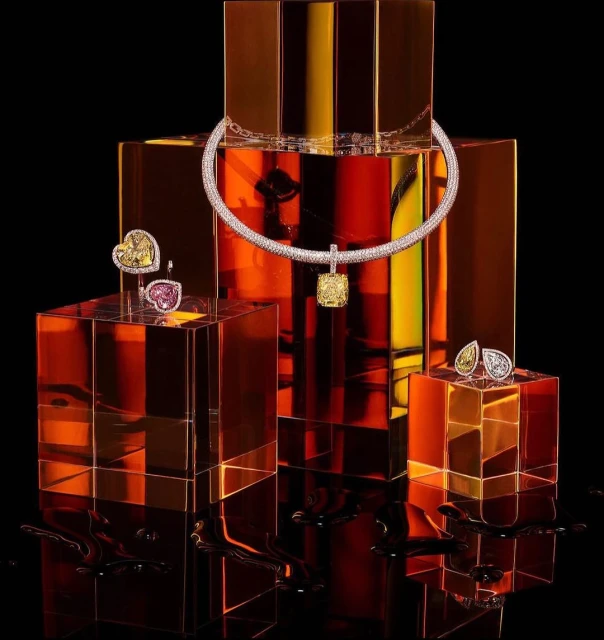 Necklace and earrings presented on translucent amber-toned blocks, in studio setting with black background. Jewellery photography.