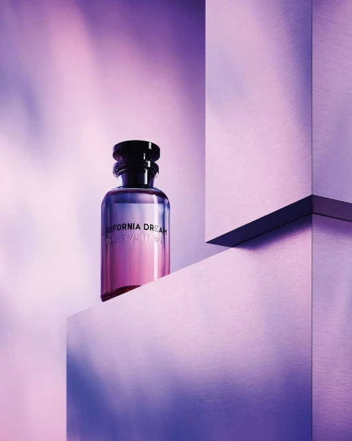 Louis Vuitton fragrance bottle featuring 'California Dream' branding, standing on violet geometric structures against a light background.