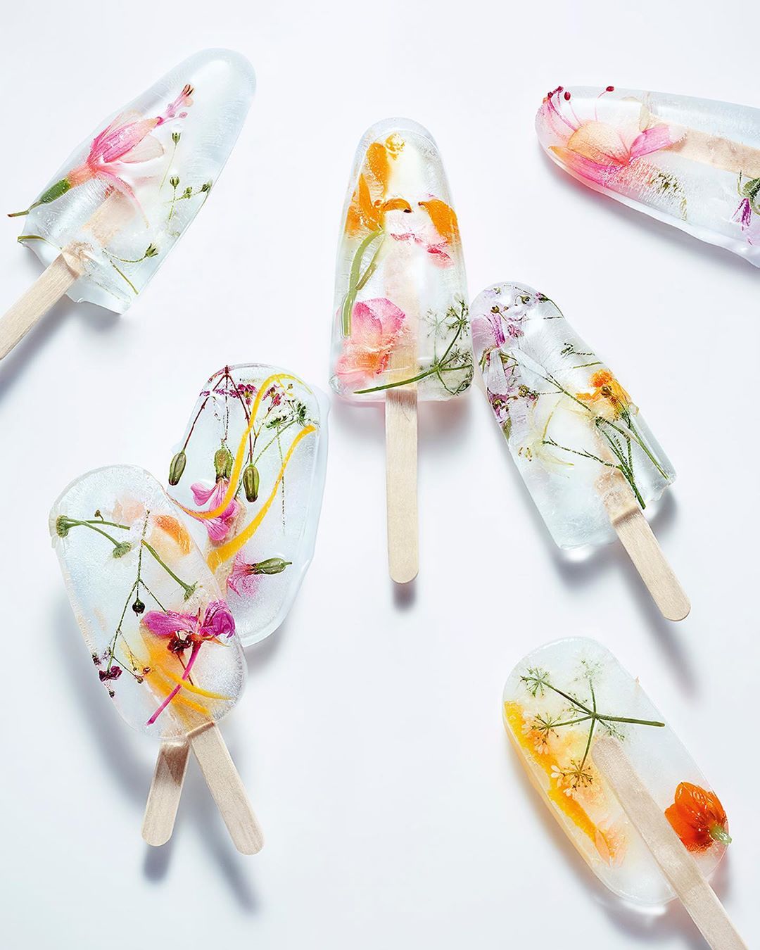 Floral ice pops on a white surface. Popsicles with frozen flowers inside. Refreshing and visually appealing frozen desserts.