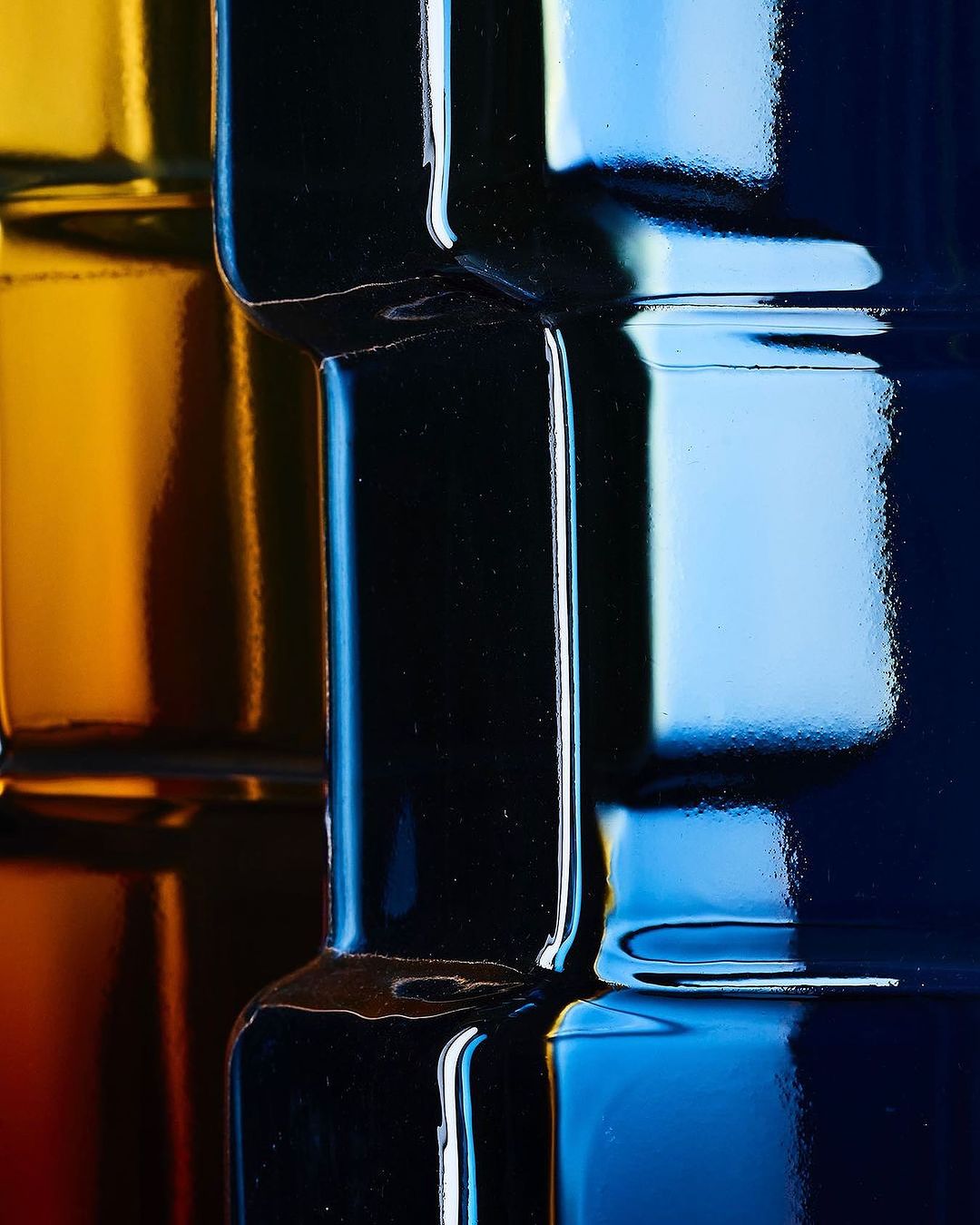 Abstract macro image of stacked, colorful glass bottles in shades of yellow, black, light blue, and dark blue, emphasizing reflections and patterns.