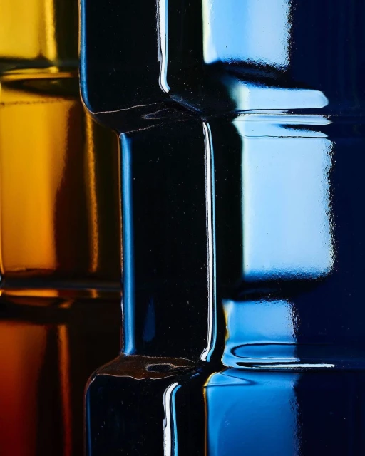 Abstract macro image of stacked, colorful glass bottles in shades of yellow, black, light blue, and dark blue, emphasizing reflections and patterns.