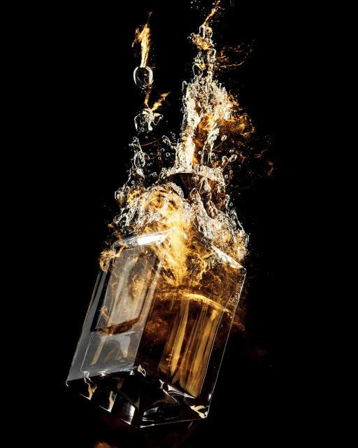 Product shot of a clear glass bottle of gold liquid with water splash effects, centered against a stark black backdrop.