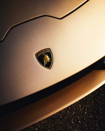 Close-up of the front of a gold Lamborghini showcasing its brand emblem on the hood, highlighting its luxury automotive design and brand identity.