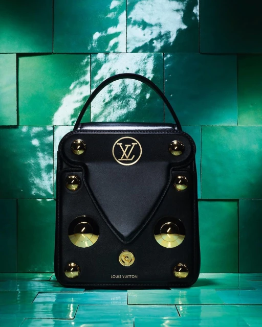 Black Louis Vuitton top-handle bag featuring gold studs and logo on a glossy teal tile background, capturing luxury and brand recognition.