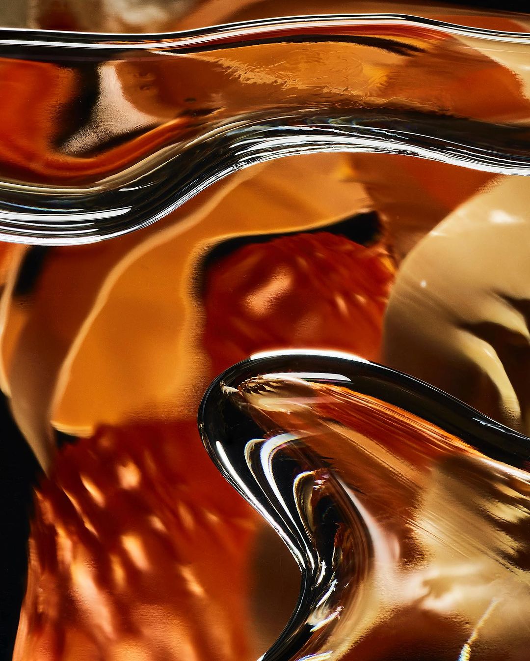 Abstract close-up of transparent glass or acrylic with an orange tint, set against a dark background, creating a fluid, organic feel.