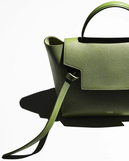 Close-up of an olive-green leather handbag with a top handle and shoulder strap against a white backdrop, emphasizing its texture and design.