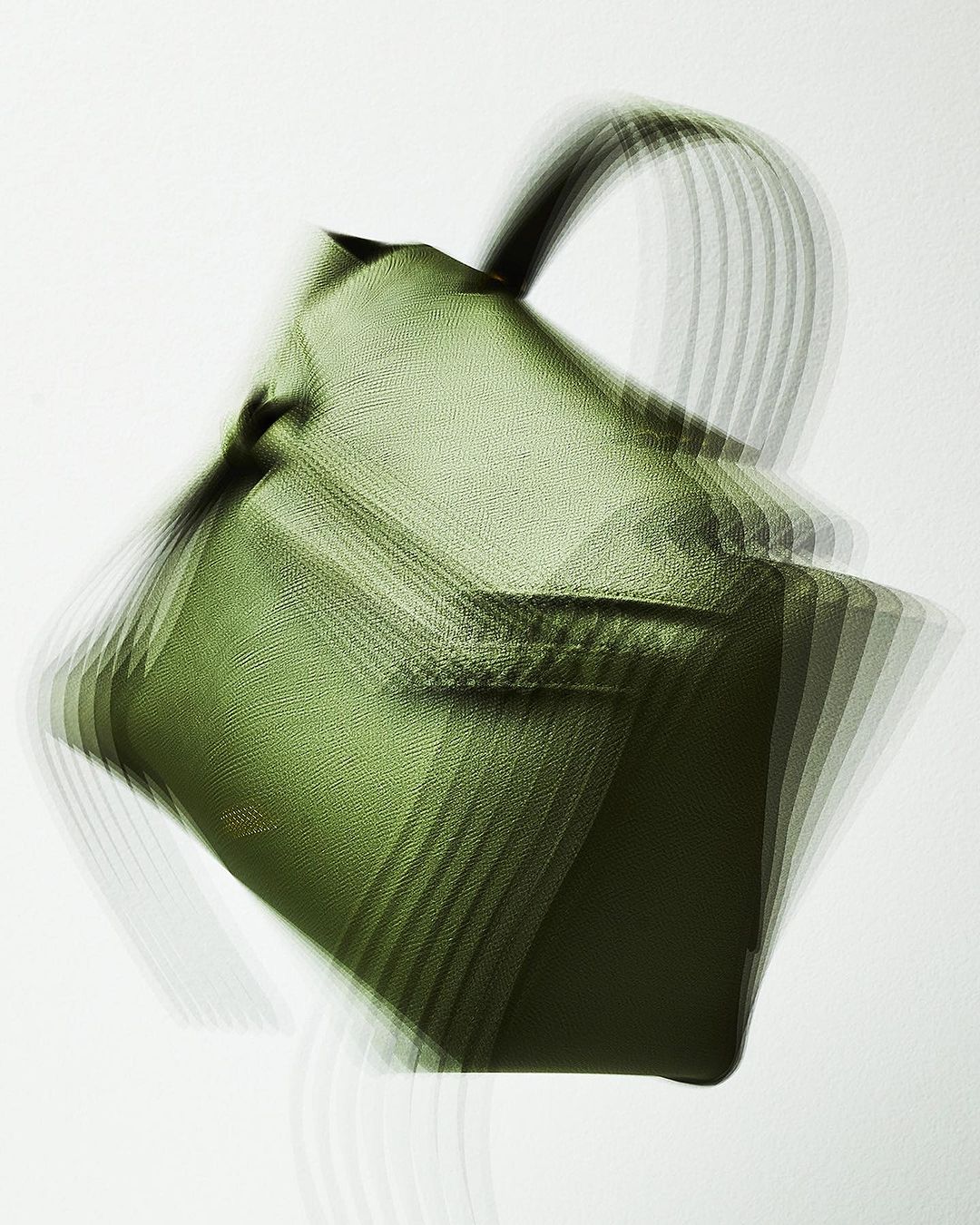 Olive green leather handbag with blurred motion effect on white background in a studio setting for a fashion product shot.