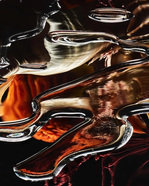 Abstract photography of curved, clear glass elements with orange and brown reflections against a dark background, creating a liquid aesthetic.