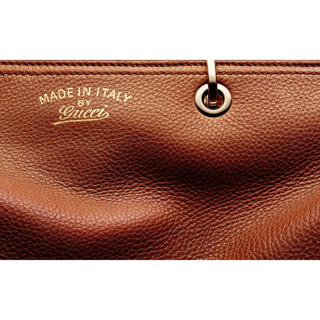 Close-up of a brown leather bag featuring gold text that reads 'MADE IN ITALY' and 'Gucci,' with a gold metal ring detail.