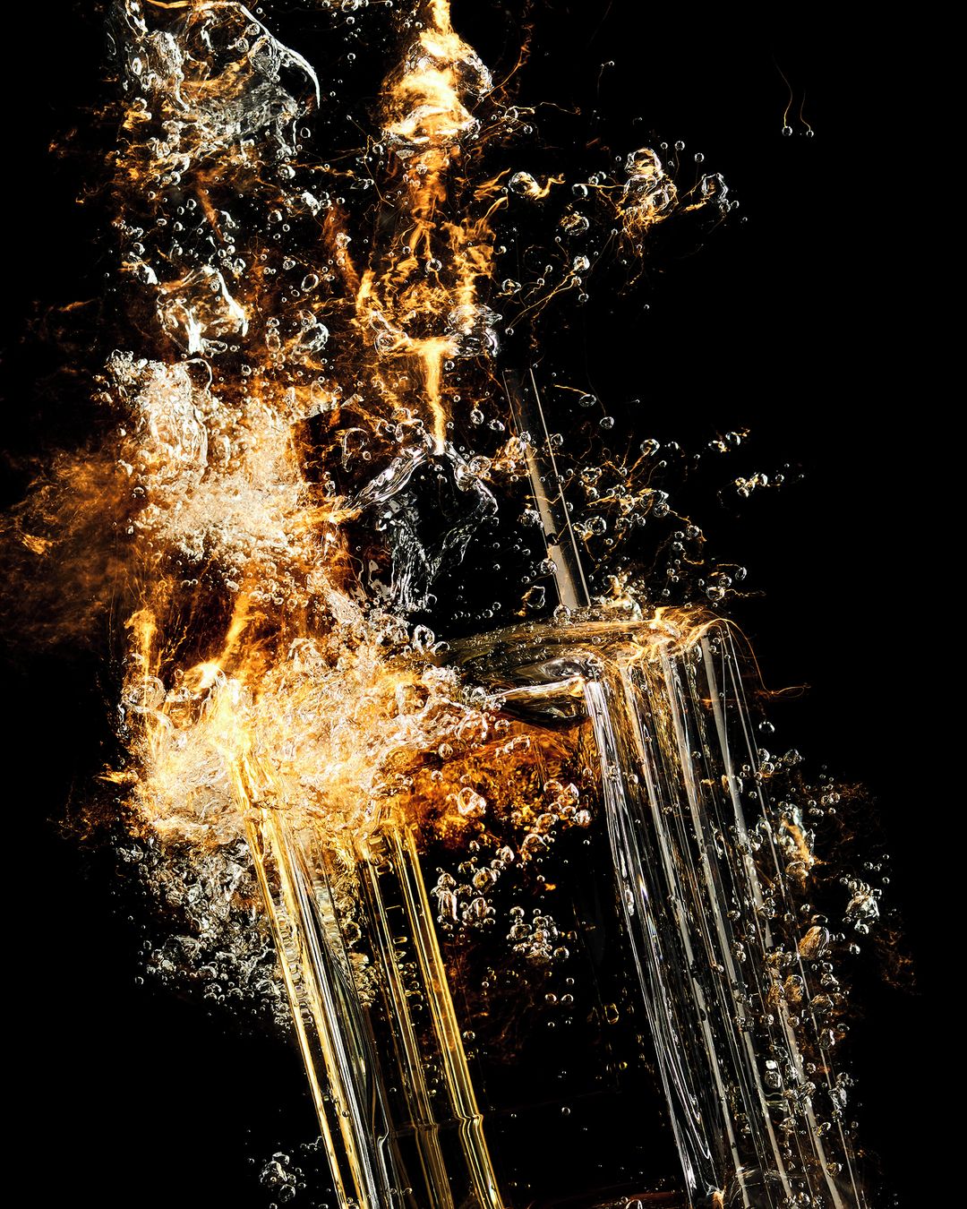 Close-up of a glass being filled with a gold colored liquid and effervescent bubbles against a black background.