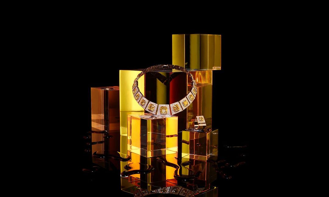 Eye-level studio shot of a yellow diamond necklace and matching ring displayed on a collection of transparent amber colored blocks.
