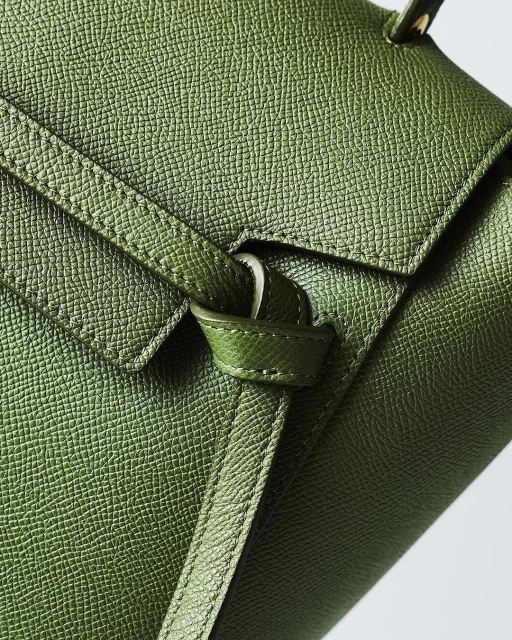 Close-up of a green leather handbag featuring a top handle, flap closure, and textured surface, providing a detailed view of the material.