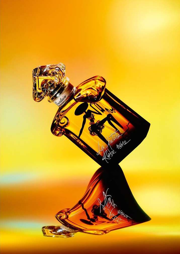 Elegant Guerlain perfume bottle angled against a gradient yellow background, reflecting its amber tones and silhouette details.