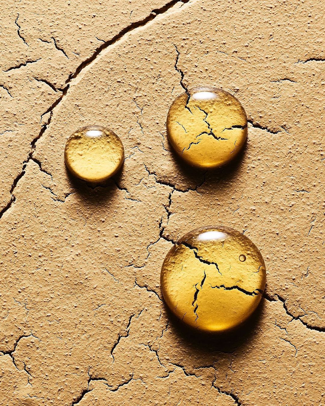 Macro studio shot of three drops of yellow liquid on a cracked surface, highlighting textures and imperfections.