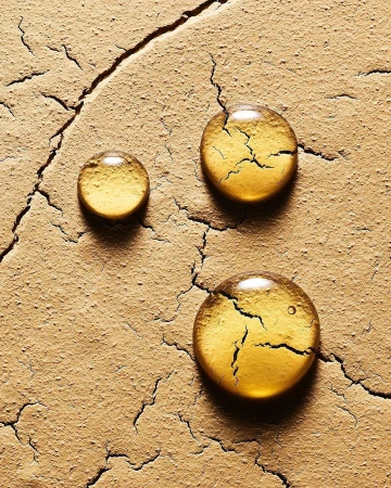 Macro studio shot of three drops of yellow liquid on a cracked surface, highlighting textures and imperfections.