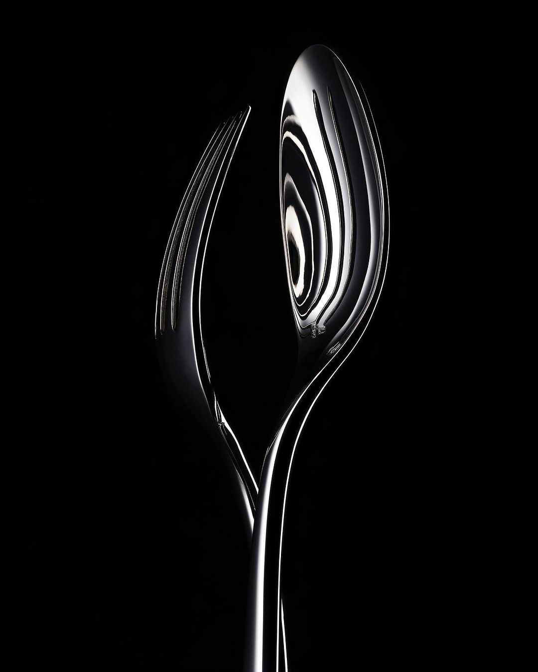 Elegant close-up of a polished silver fork and spoon intertwined against a stark black background in a studio lighting setup.