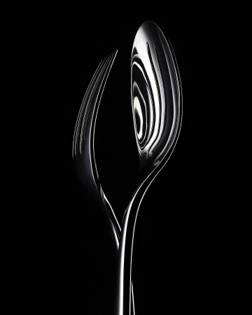 Elegant close-up of a polished silver fork and spoon intertwined against a stark black background in a studio lighting setup.