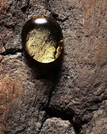 Textured stone surface with a single, clear water droplet reflecting the surface beneath it, creating an abstract and natural composition.