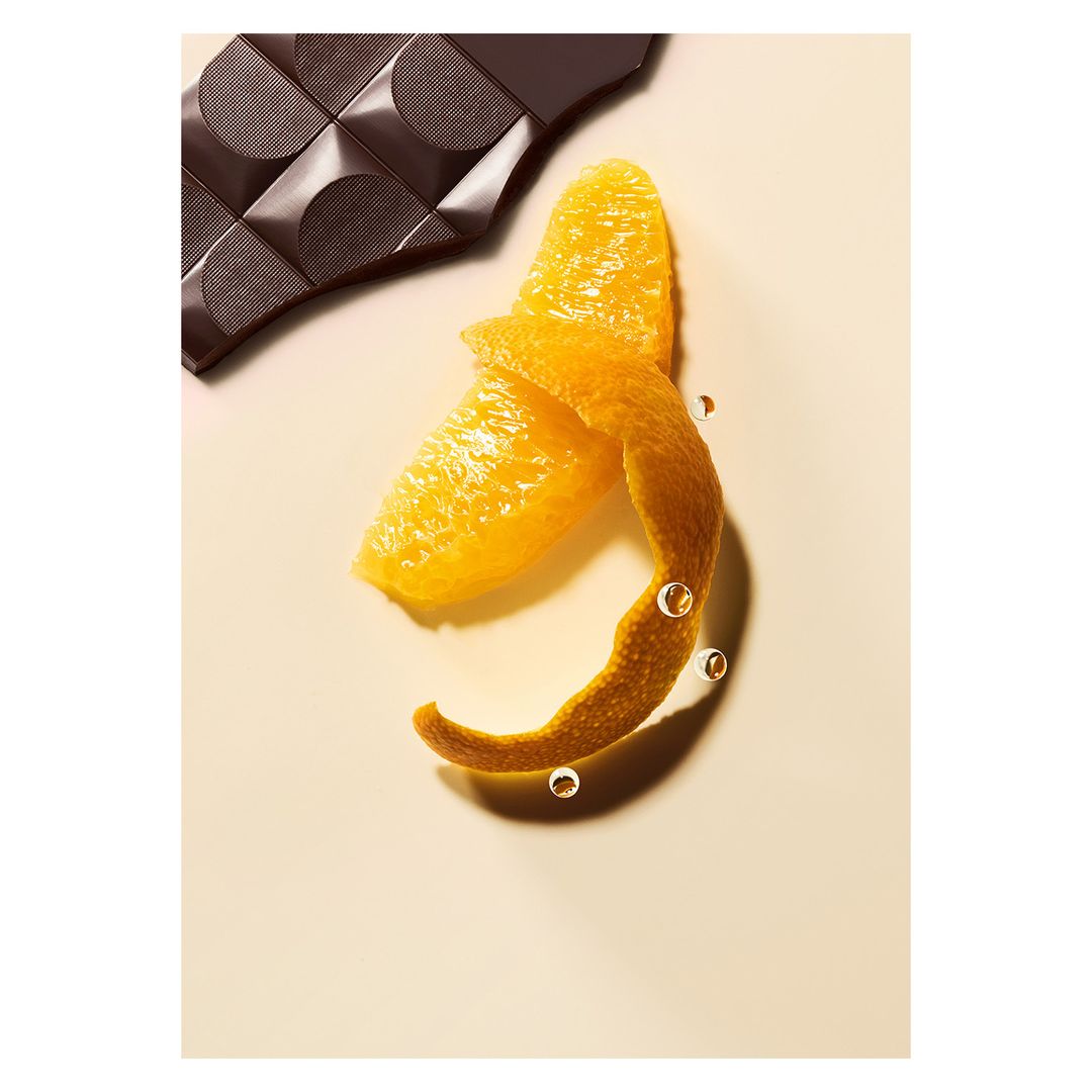 Studio shot featuring dark chocolate pieces, peeled orange, and water droplets on a light background. Food and beverage photography.