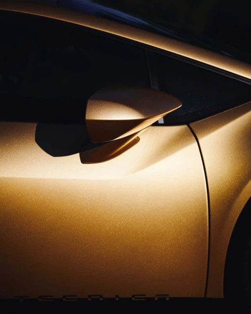 Close-up of a gold-colored automotive exterior featuring a side mirror, door, and window, highlighting the sleek design and reflective surface.