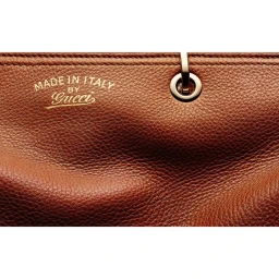 Macro shot of brown leather handbag texture with gold foil stamped logo and metal ring hardware