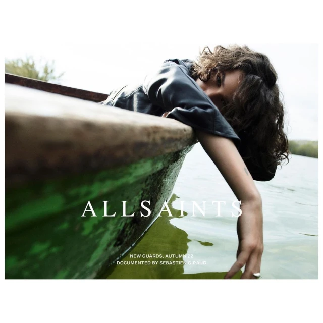 Fashion shot featuring a young adult female model in a boat on a lake, wearing a black jacket for All Saints. 