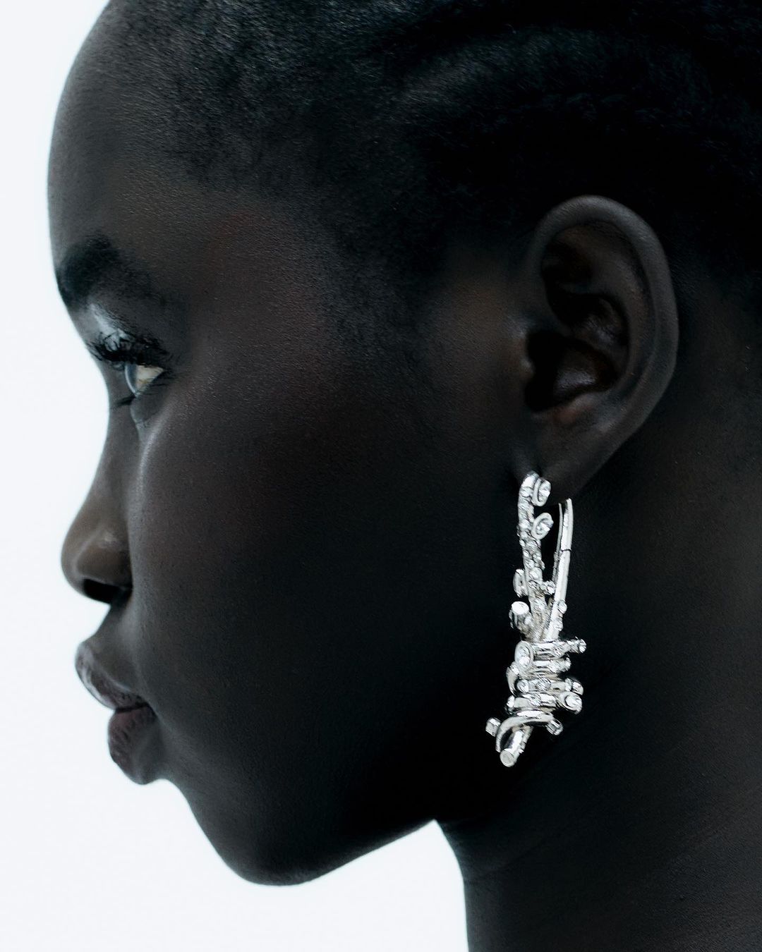 Close-up profile of Black woman wearing artistic silver earrings. Fashion shot against white background.