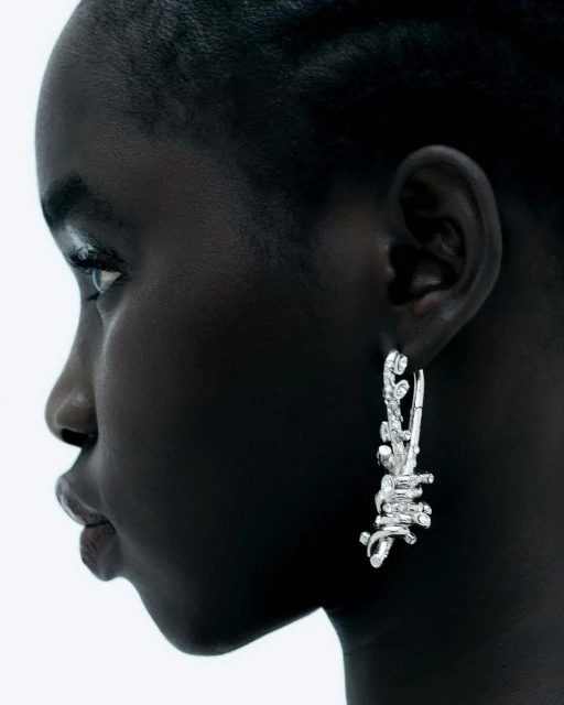 Close-up profile of Black woman wearing artistic silver earrings. Fashion shot against white background.