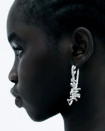 Close-up profile of Black woman wearing artistic silver earrings. Fashion shot against white background.