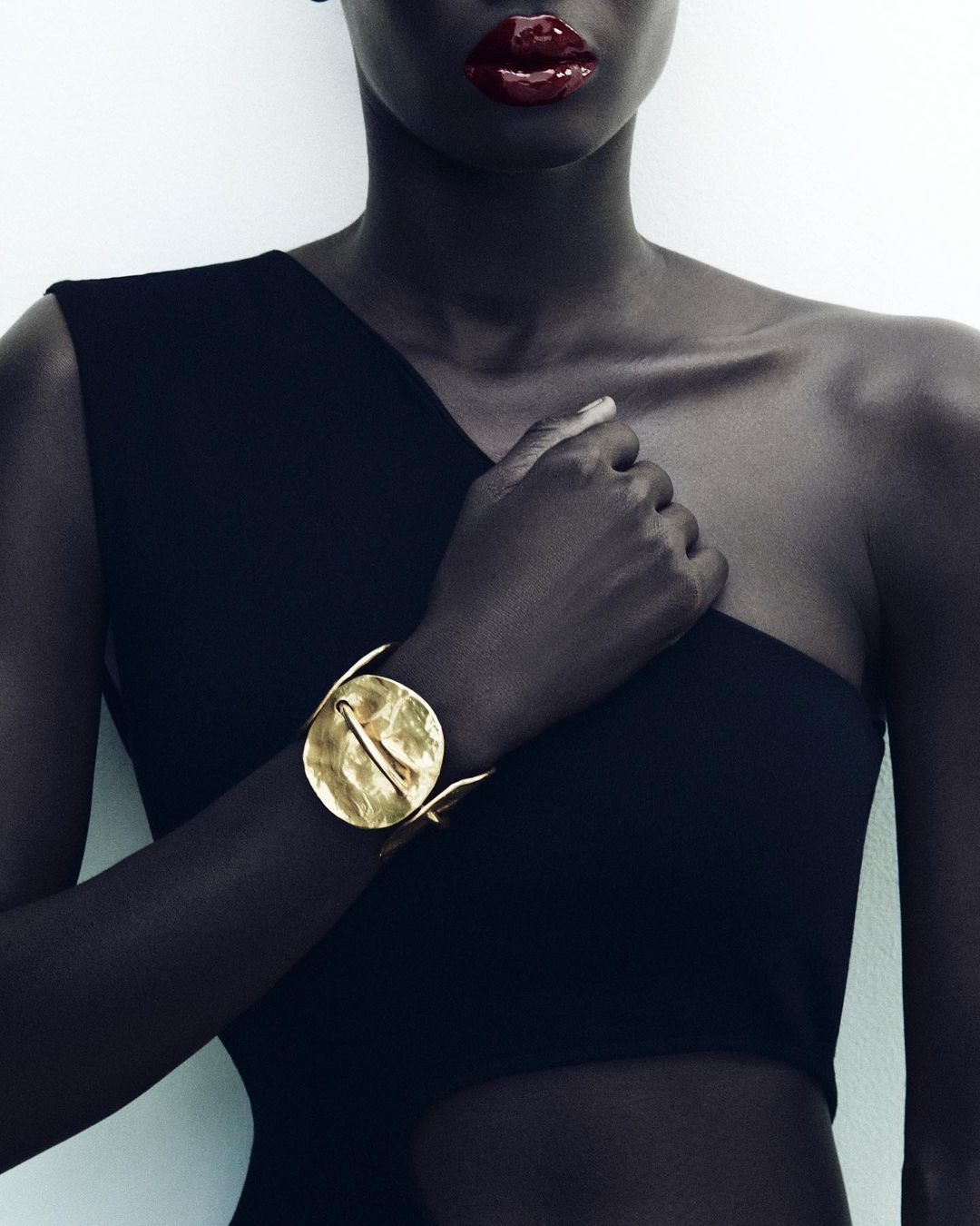 Elegant portrait of an African American woman showcasing a gold cuff bracelet against a white background and black dress.