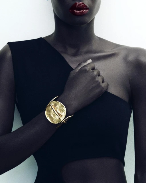 Elegant portrait of an African American woman showcasing a gold cuff bracelet against a white background and black dress.