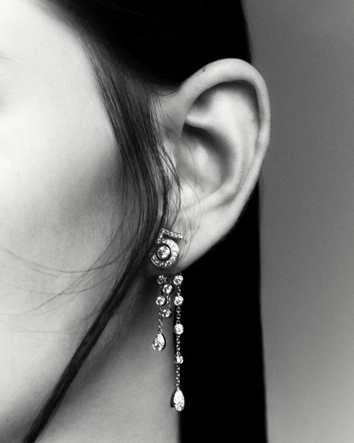 Close-up studio shot of an adult woman's ear wearing diamond 'number 5' earrings with a grey background in monochrome.