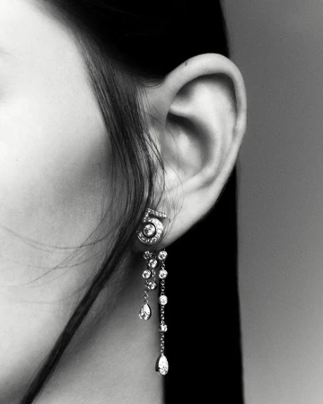 Close-up studio shot of an adult woman's ear wearing diamond 'number 5' earrings with a grey background in monochrome.