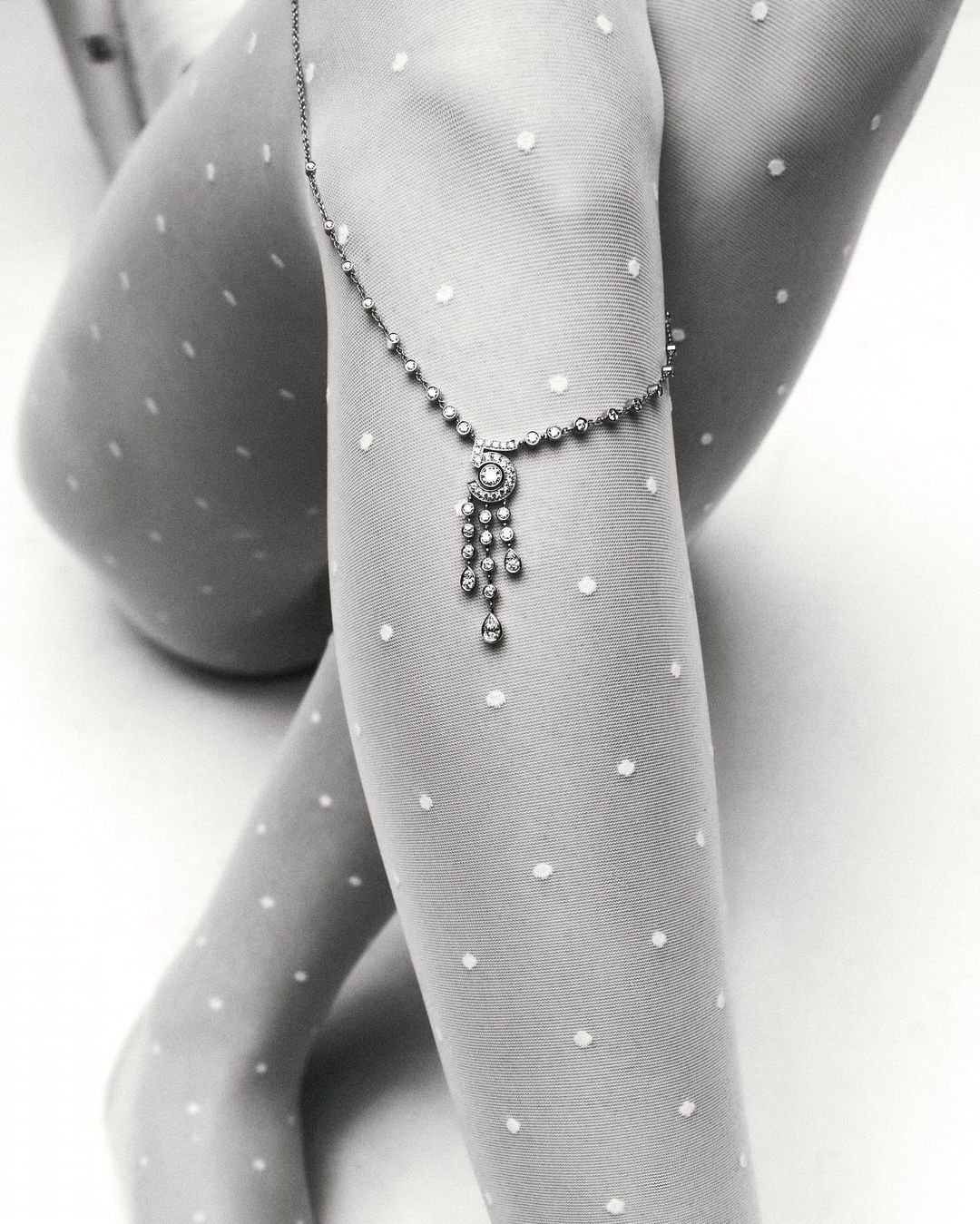 Close-up studio shot of a woman's legs adorned with a delicate jeweled anklet over polka dot tights, creating a sophisticated visual.