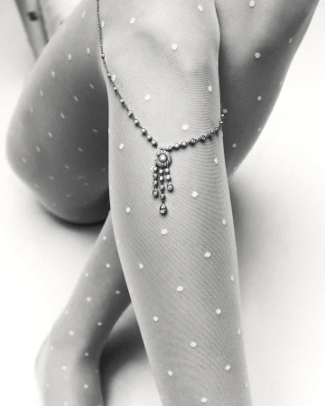 Close-up studio shot of a woman's legs adorned with a delicate jeweled anklet over polka dot tights, creating a sophisticated visual.