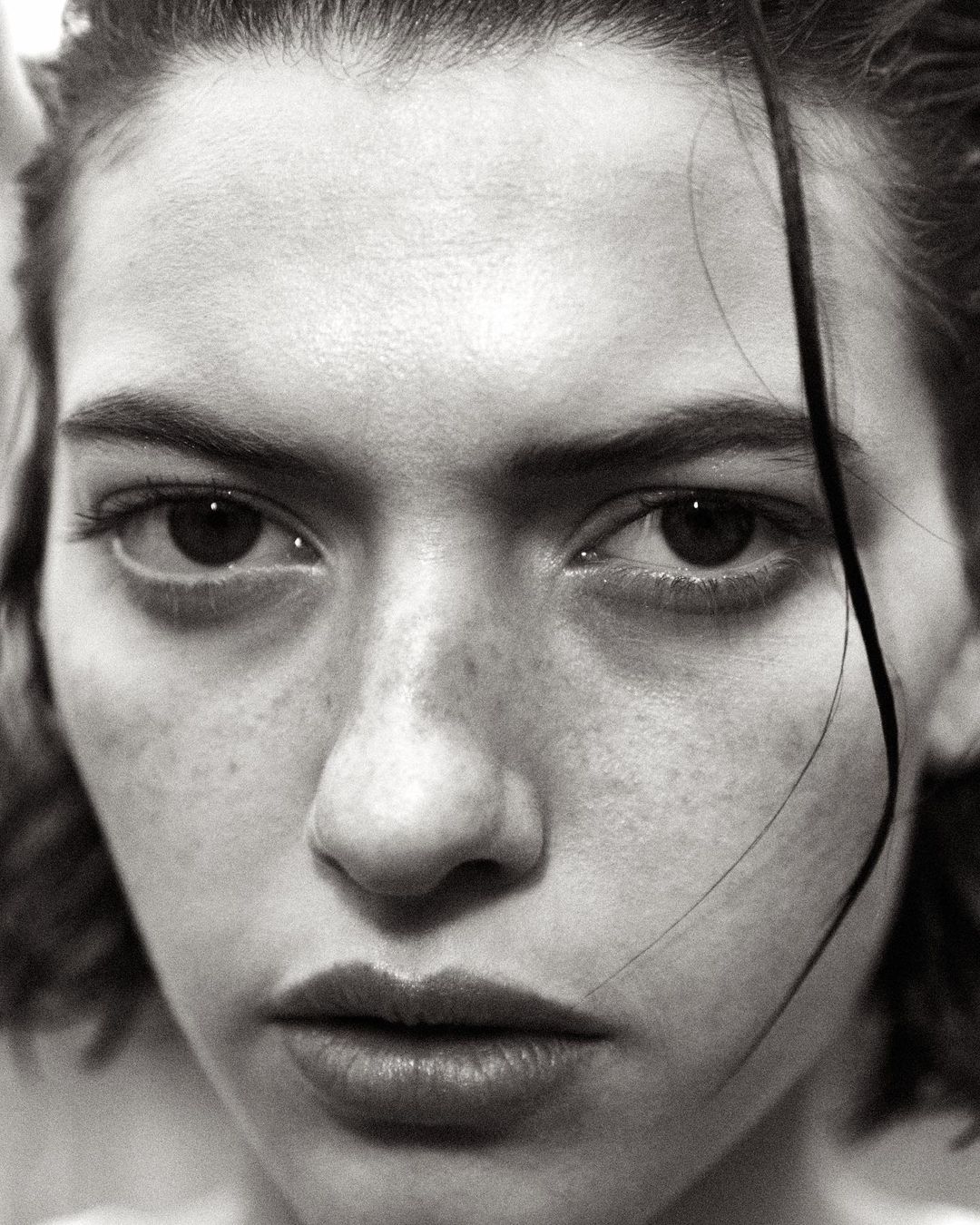 Close-up monochrome portrait of a young woman with wet hair framing her face and freckles across her nose.