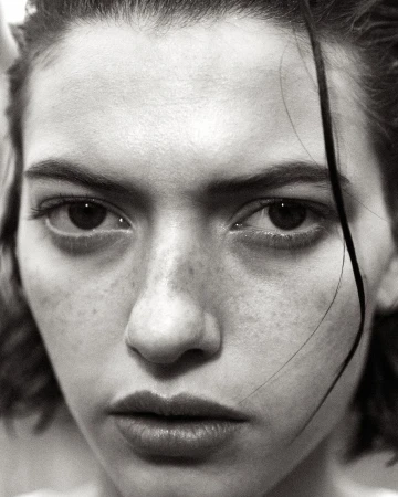 Close-up monochrome portrait of a young woman with wet hair framing her face and freckles across her nose.