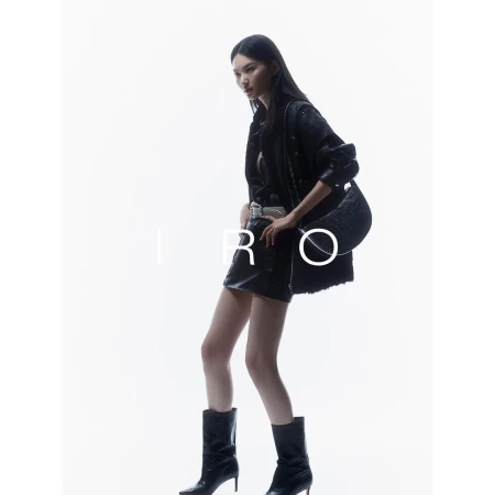 Model in black leather jacket and miniskirt holding a black handbag against a bright white seamless background