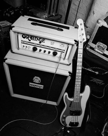 Monochrome image of a bass guitar next to an amplifier on a dark surface, evoking a vintage music scene in a studio setting.