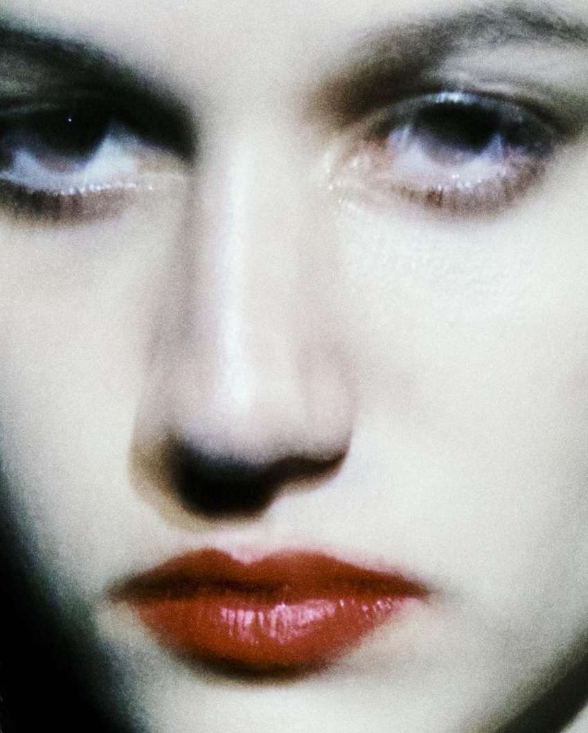 Close-up studio shot of a woman's face with focus on bright red lips, pale skin, and dark eyes. Cosmetics and beauty concept.