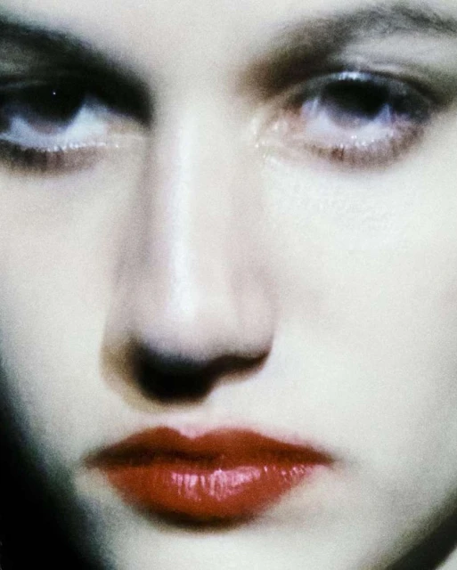 Close-up studio shot of a woman's face with focus on bright red lips, pale skin, and dark eyes. Cosmetics and beauty concept.