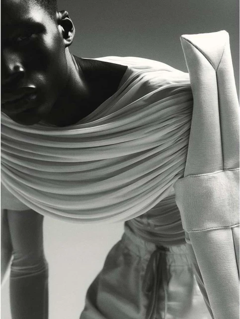 Monochromatic fashion shot featuring a Black male model wearing draped, structured white fabric, posing against a neutral backdrop.
