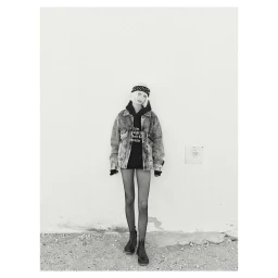 Monochrome fashion portrait of a model wearing a distressed denim jacket, black hoodie, headband, and boots.