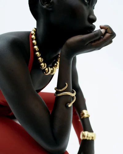 Close-up fashion portrait of a Black woman wearing gold jewelry and red clothing against a plain white background