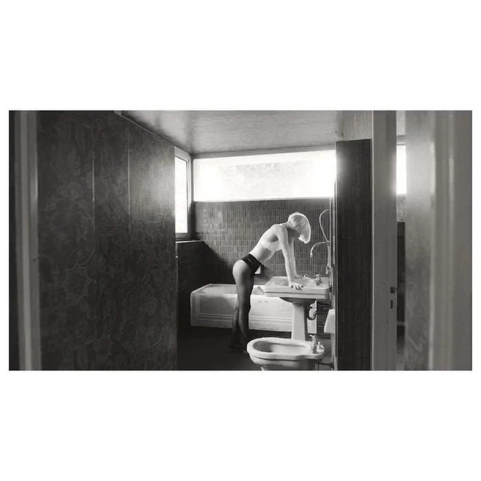 Monochrome portrait of a woman leaning over a bathroom sink in a vintage tiled interior by Sebastien Giraud